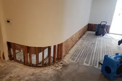 Lower drywall removed and a dehumidifier running in a water-damaged room