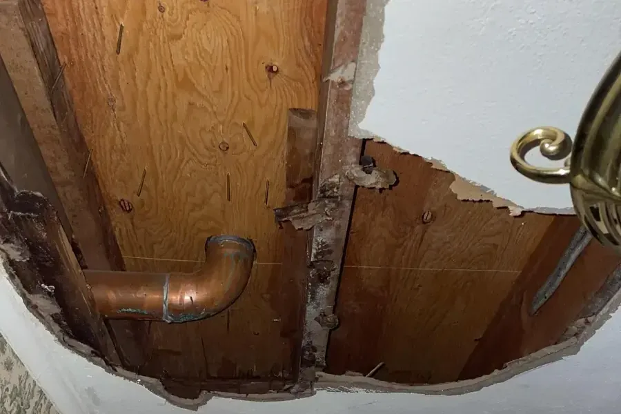 A ceiling opened to reach a leaking copper drain pipe